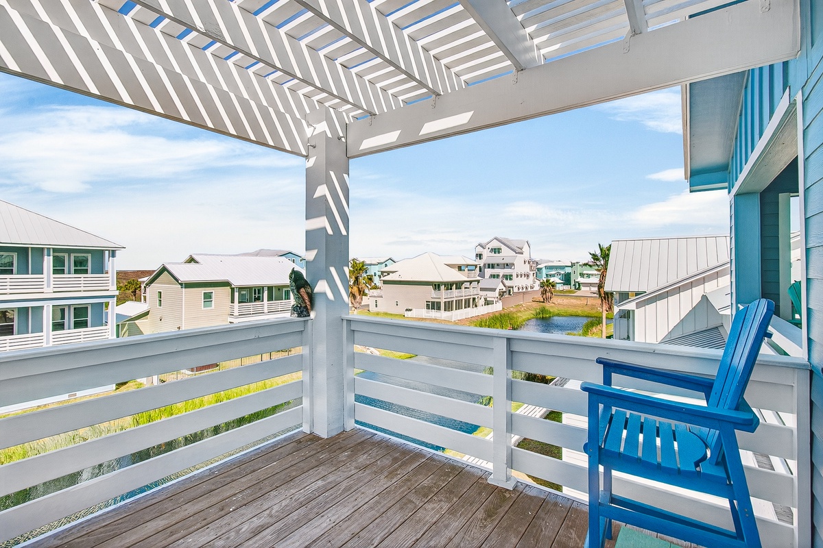 Relax on your private deck with pergola shade and blue coastal chairs, overlooking charming neighborhood homes and peaceful water views.