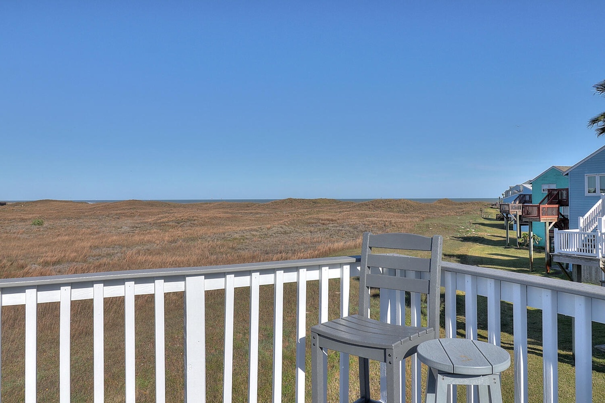Elevated coastal home with expansive views across pristine marshlands and neighboring beach houses under endless blue skies.