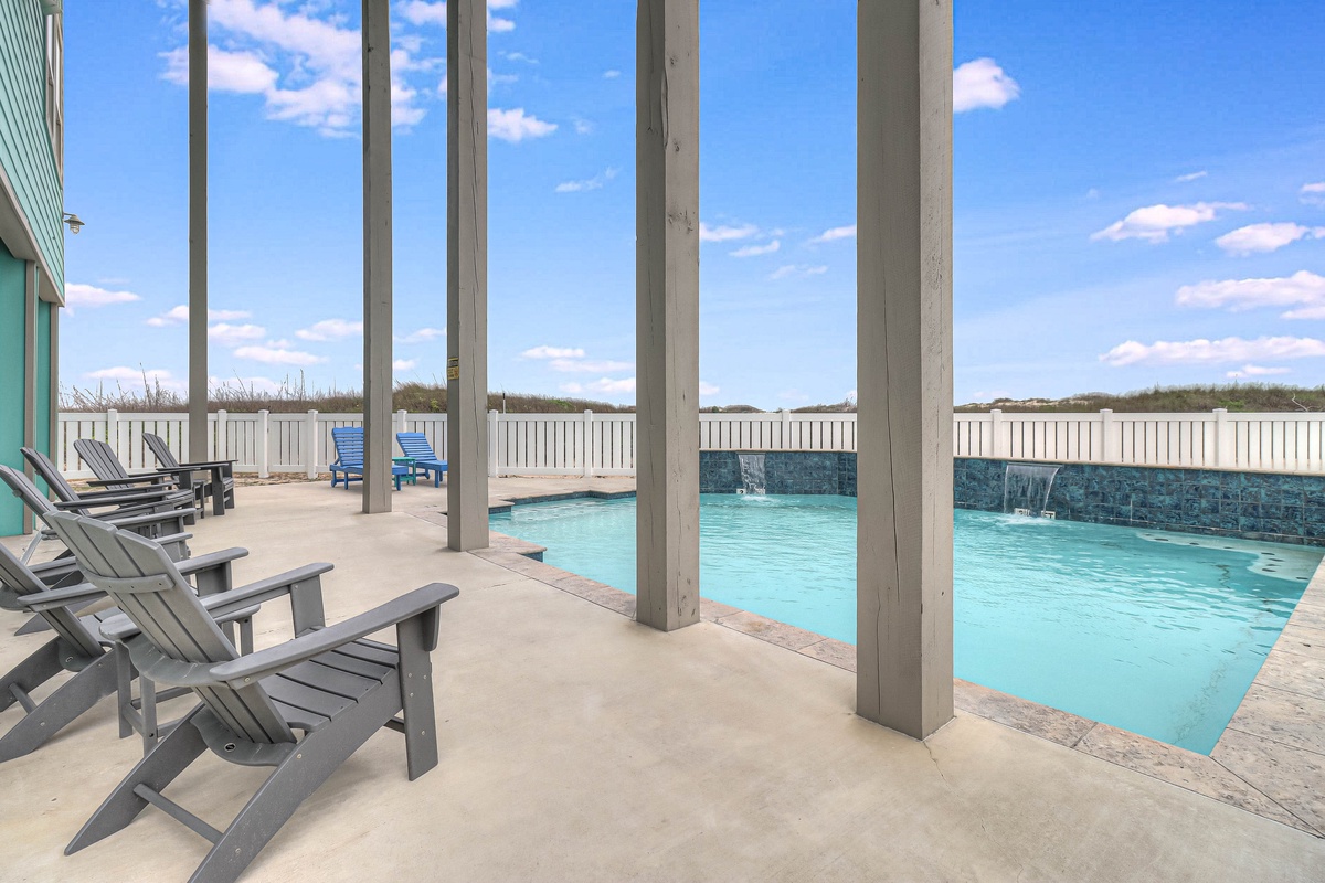 Unwind poolside under the shaded pergola with comfortable lounge chairs overlooking crystal-clear waters and coastal views.