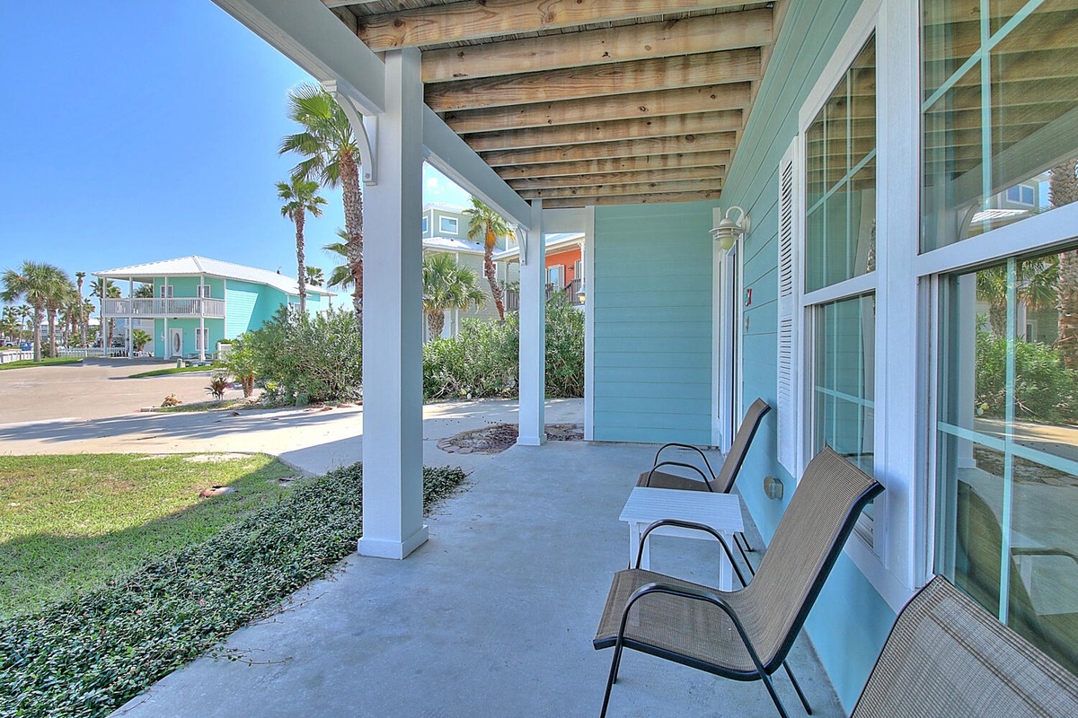 Relax on your private covered patio with comfortable seating, surrounded by tropical palms and colorful beach cottages in this peaceful resort setting.