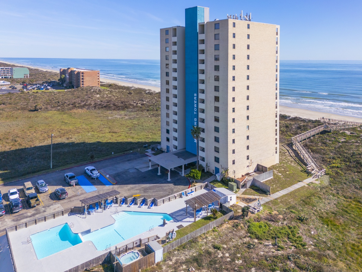 Beachfront tower offering stunning ocean views with pool, parking, and direct beach access via wooden walkway.