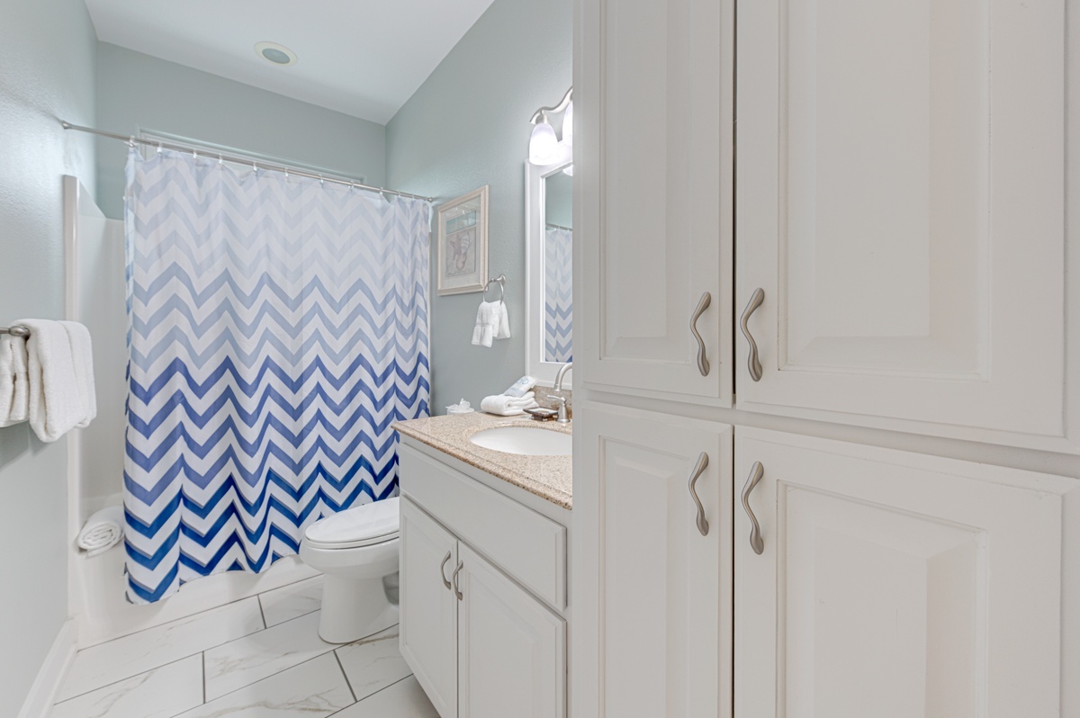 Refresh in your elegant bathroom featuring marble countertops, plenty of storage, and a calming blue chevron shower curtain.
