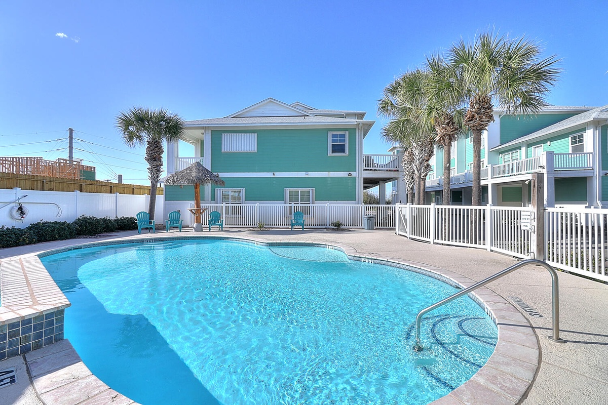Tropical vacation rental complex featuring sparkling pool, palm trees, and colorful beachside architecture under clear blue skies.