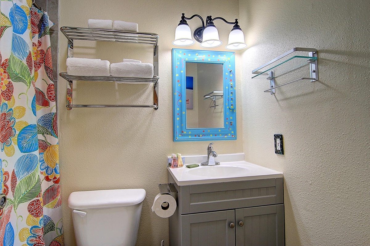 Your bright bathroom features a colorful mirror and chrome shelving for towels, creating a cheerful space to freshen up.