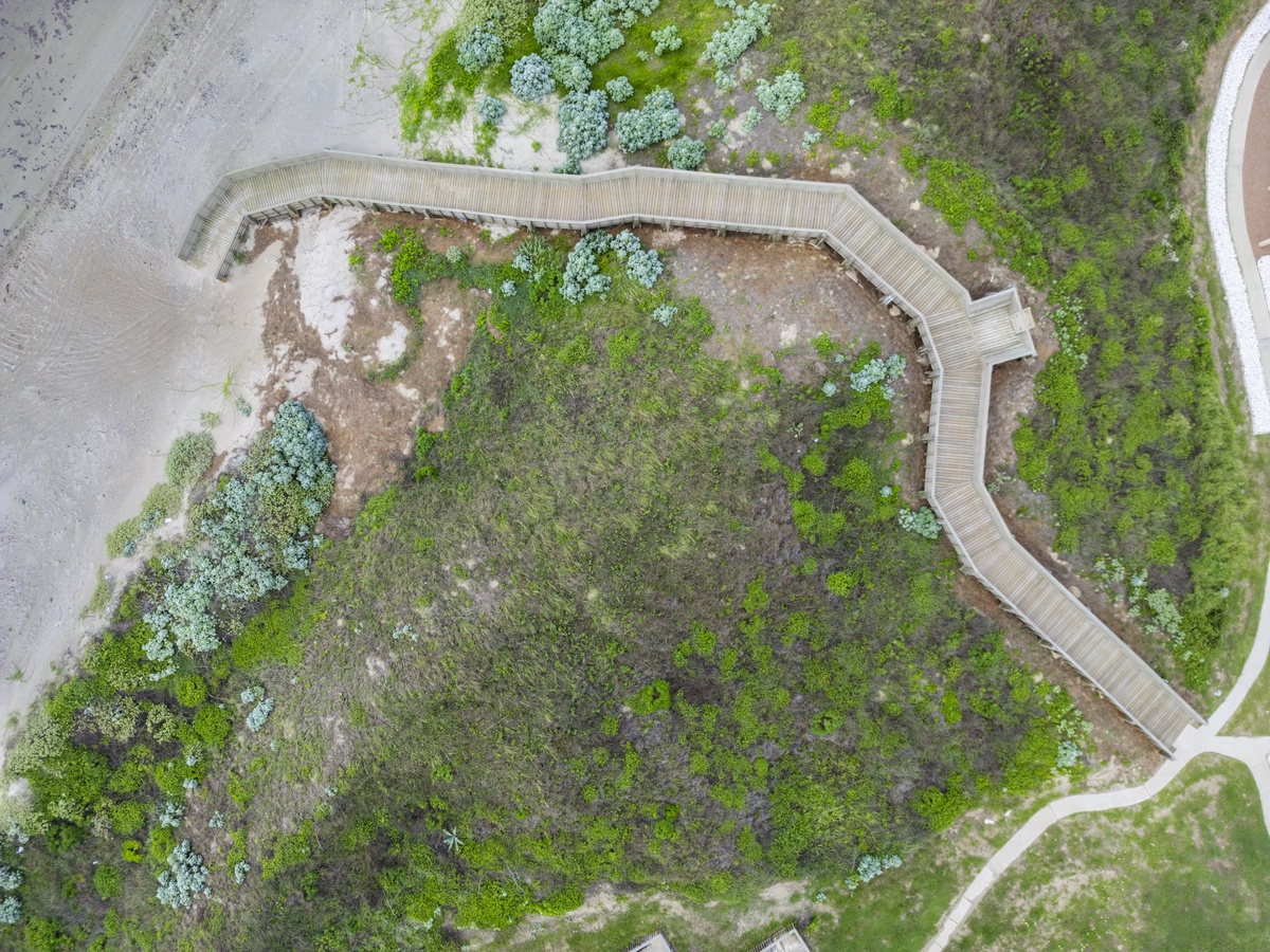 Aerial view reveals a winding boardwalk through natural vegetation and coastal landscape near the property.