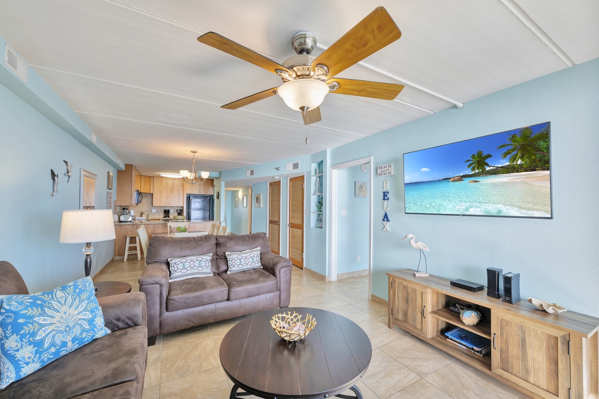 Unwind in your coastal-themed living space with comfortable seating, ceiling fan, and tropical artwork that sets the perfect beach getaway mood.