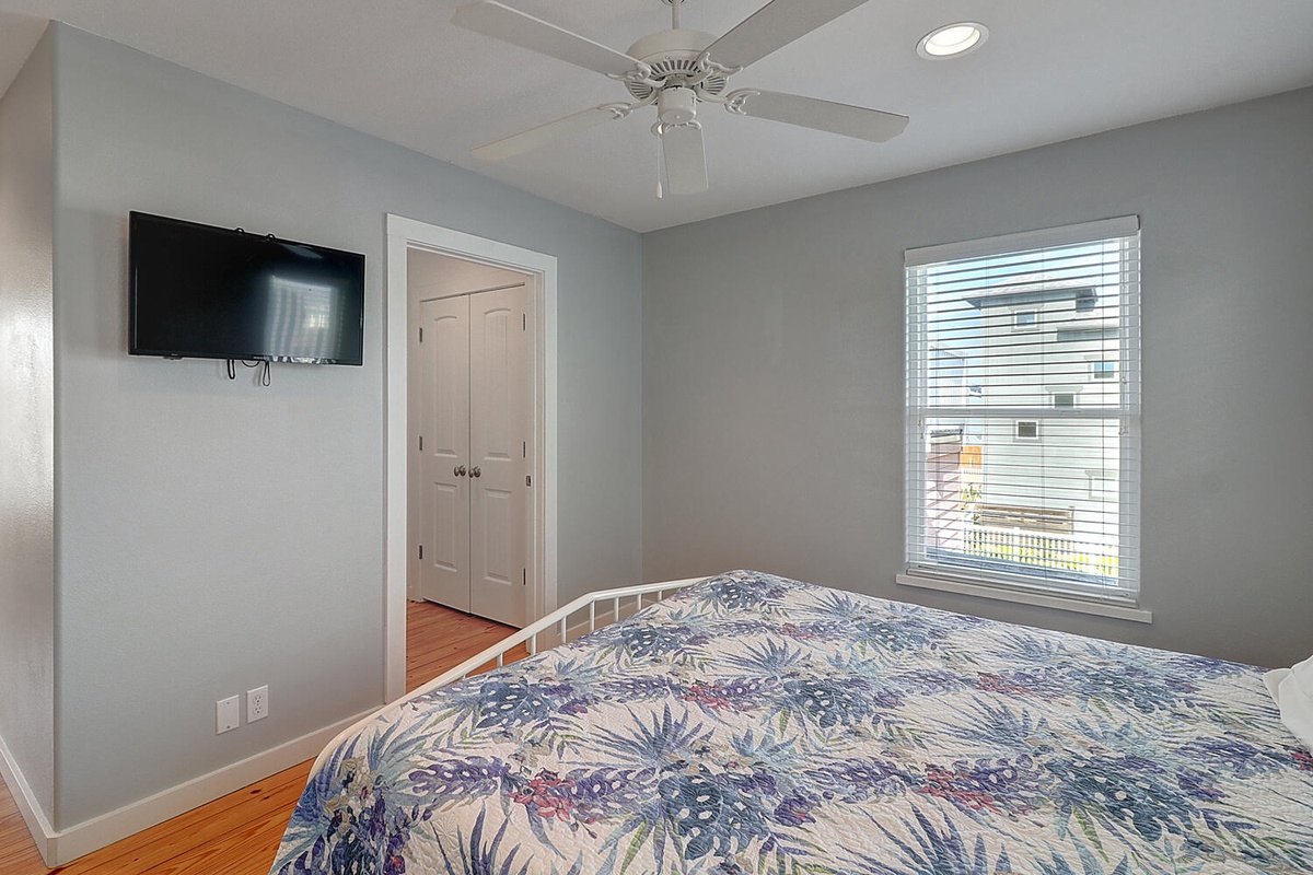 Unwind in your peaceful bedroom with soft gray walls, tropical bedding, and wall-mounted TV for cozy evenings.