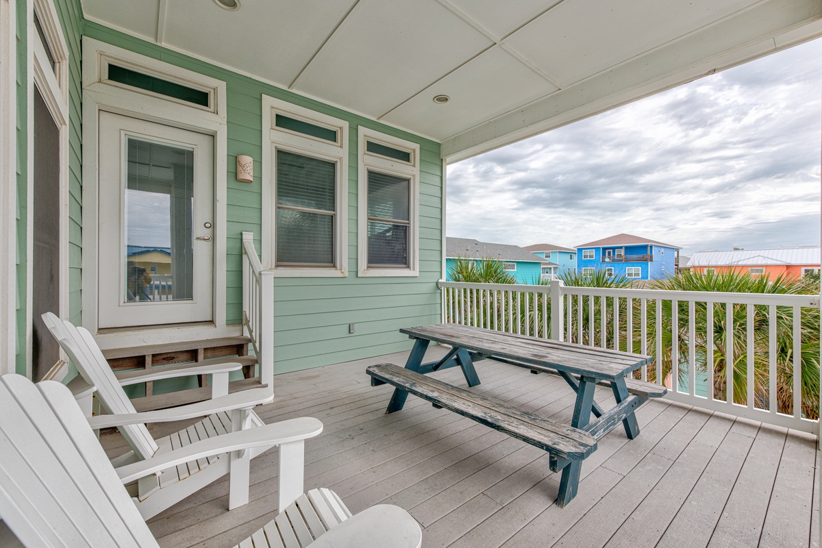 Your spacious covered deck offers peaceful moments with Adirondack chairs and picnic table, framed by colorful coastal homes.