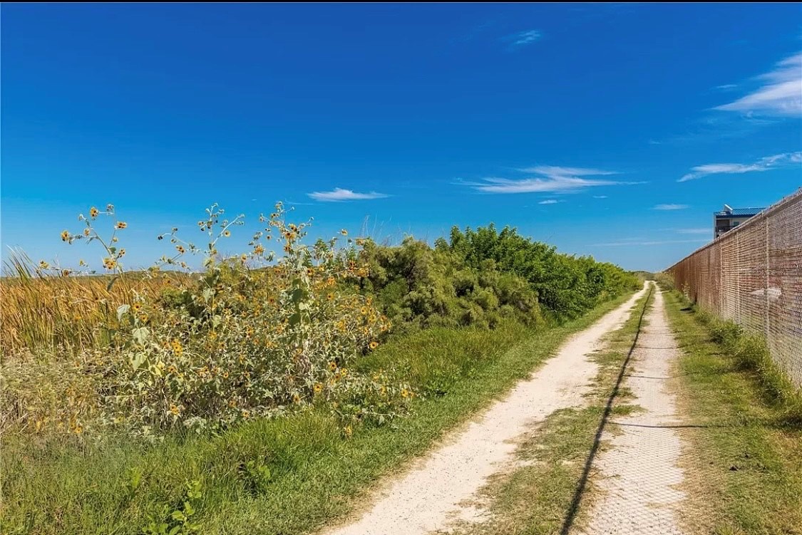 Rural walking path leads through peaceful countryside with wildflowers and traditional brick walls under brilliant blue skies.