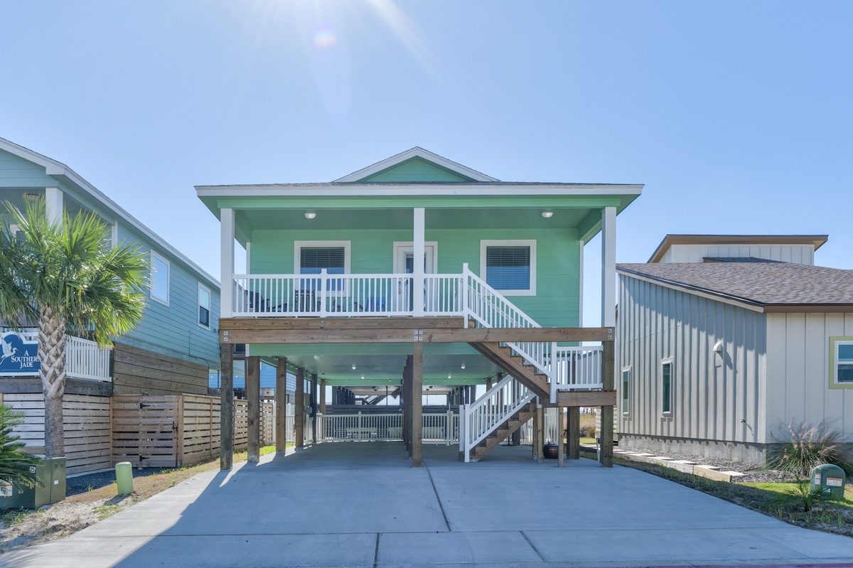 Bright green coastal home with covered parking and elevated deck in sunny beachside neighborhood.