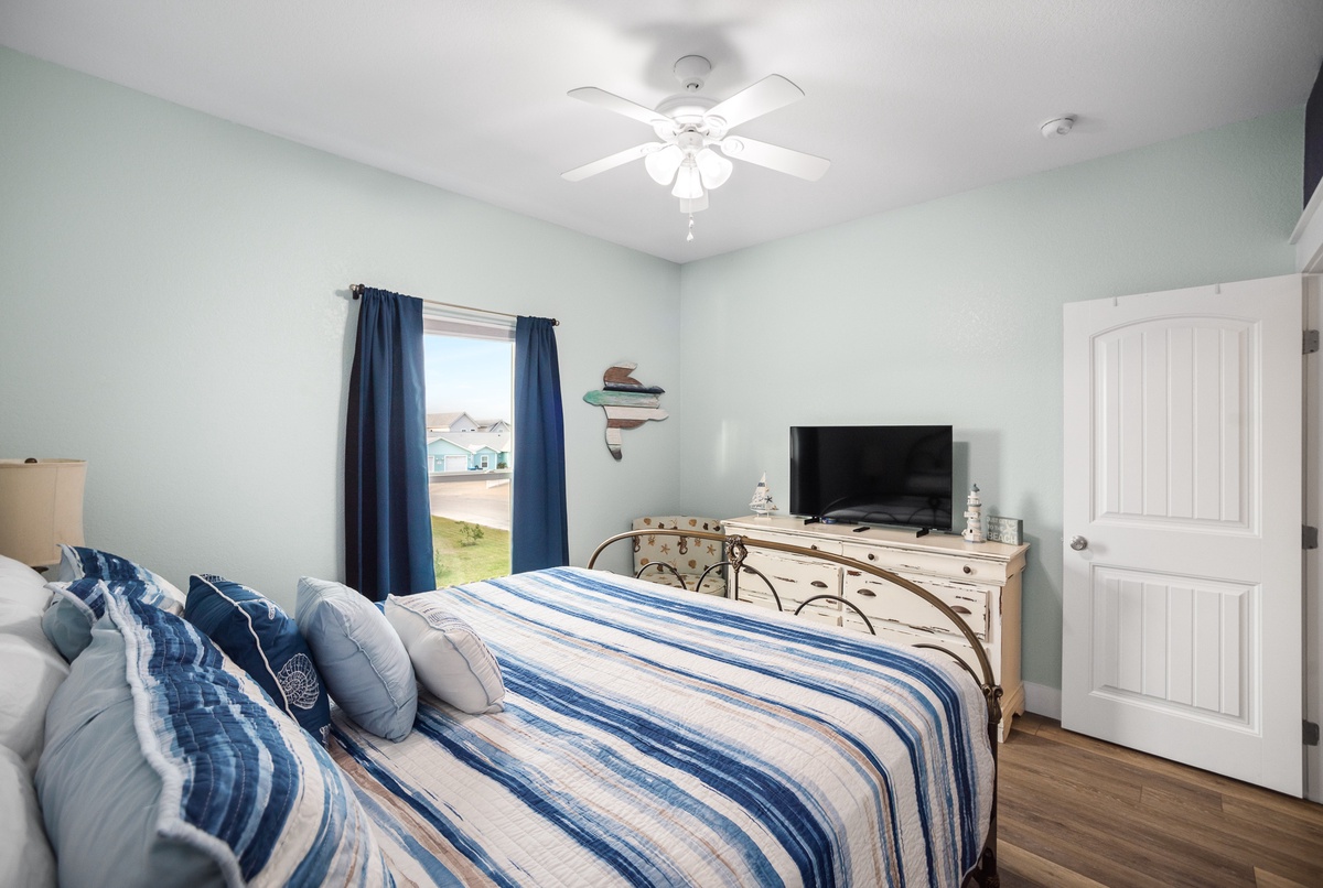 Relax in your peaceful bedroom with coastal-inspired decor, featuring a comfortable bed, ceiling fan, and TV for unwinding after your adventures.