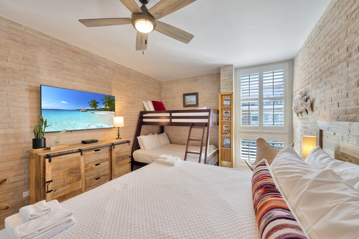 Your cozy bedroom features a plush bed, bunk beds for extra guests, and rustic brick walls that create a warm, inviting atmosphere.