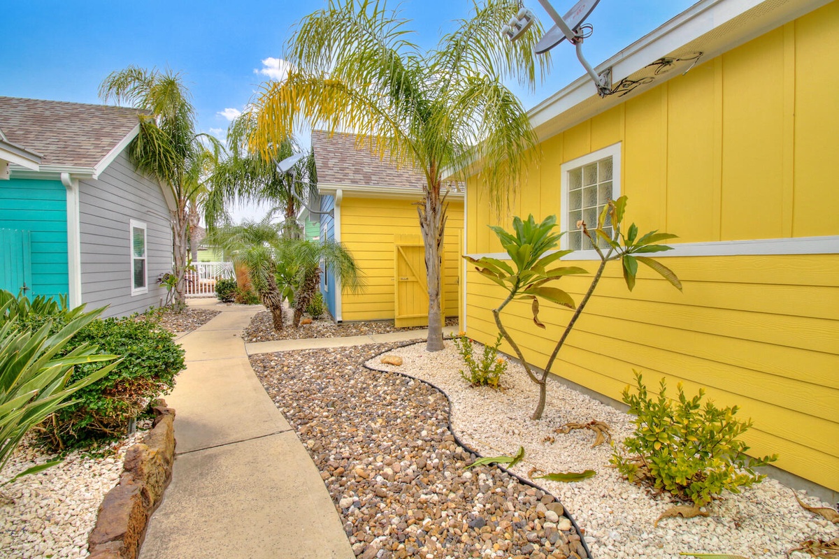 Colorful tropical cottages with vibrant yellow and turquoise exteriors surrounded by lush palm trees and tropical landscaping.