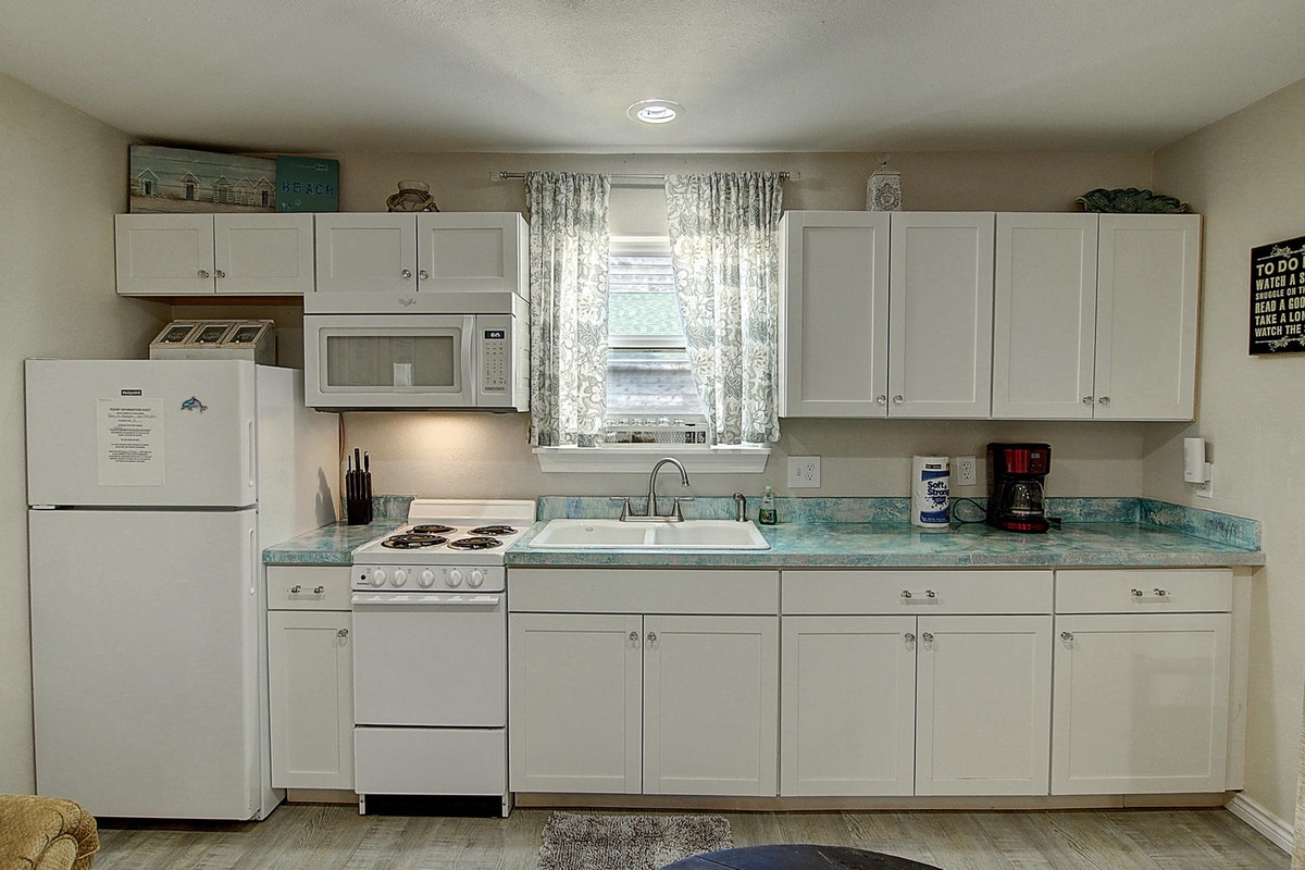 Your fully equipped kitchen awaits with turquoise countertops, white appliances, and charming window views for memorable meal preparation.