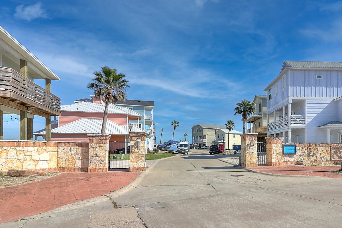 Coastal community entrance with palm trees and colorful beach houses creating a welcoming seaside atmosphere.