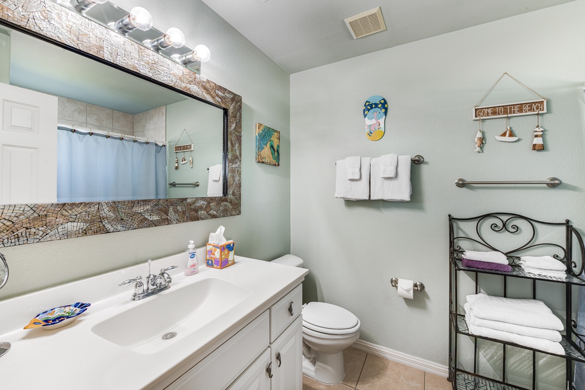 Your coastal-themed bathroom awaits with soft blue walls, beach décor, and fluffy towels neatly arranged for your comfort.
