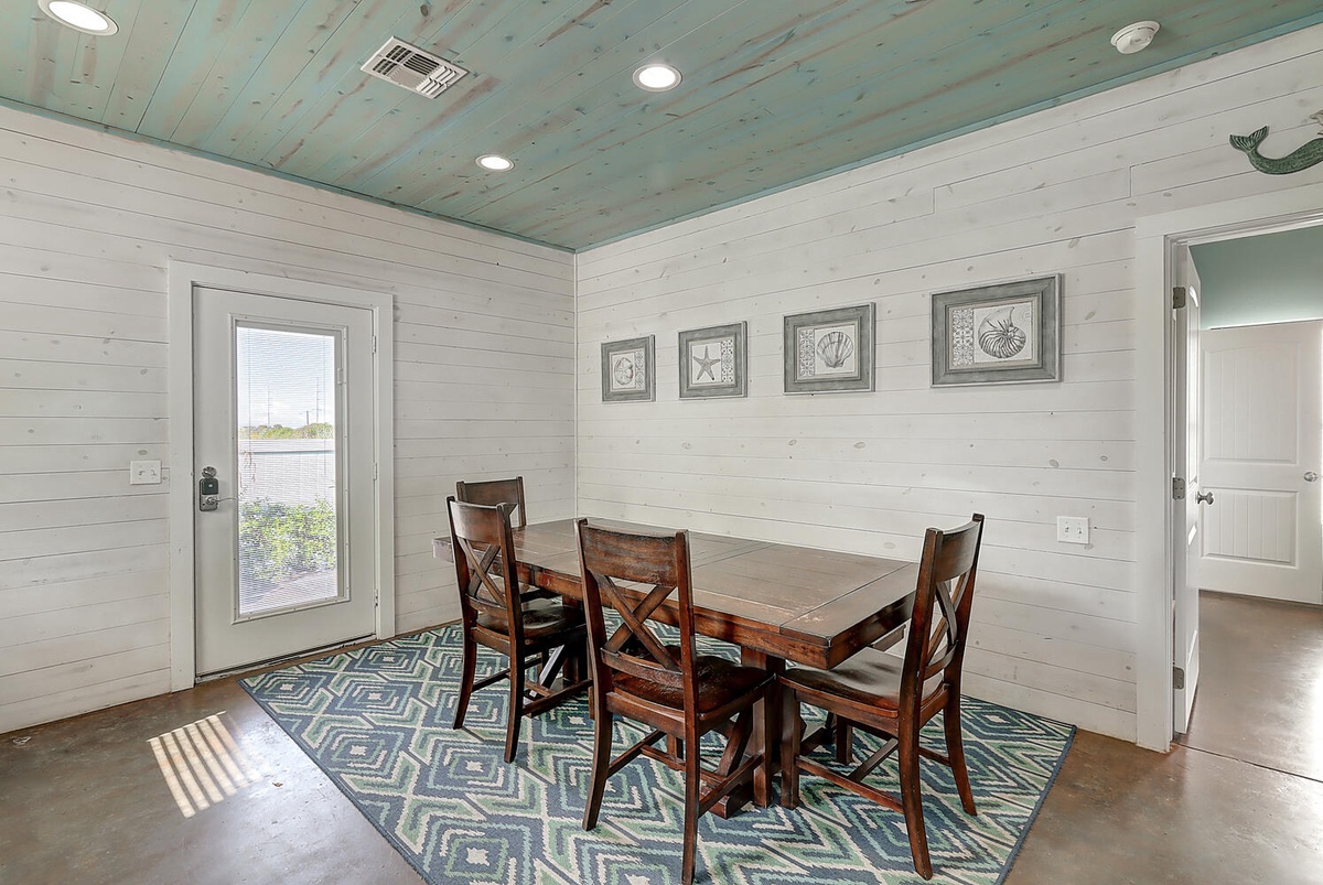 Your coastal dining room features rustic wooden table, beachy blue ceiling, and charming seashell artwork for memorable meals.