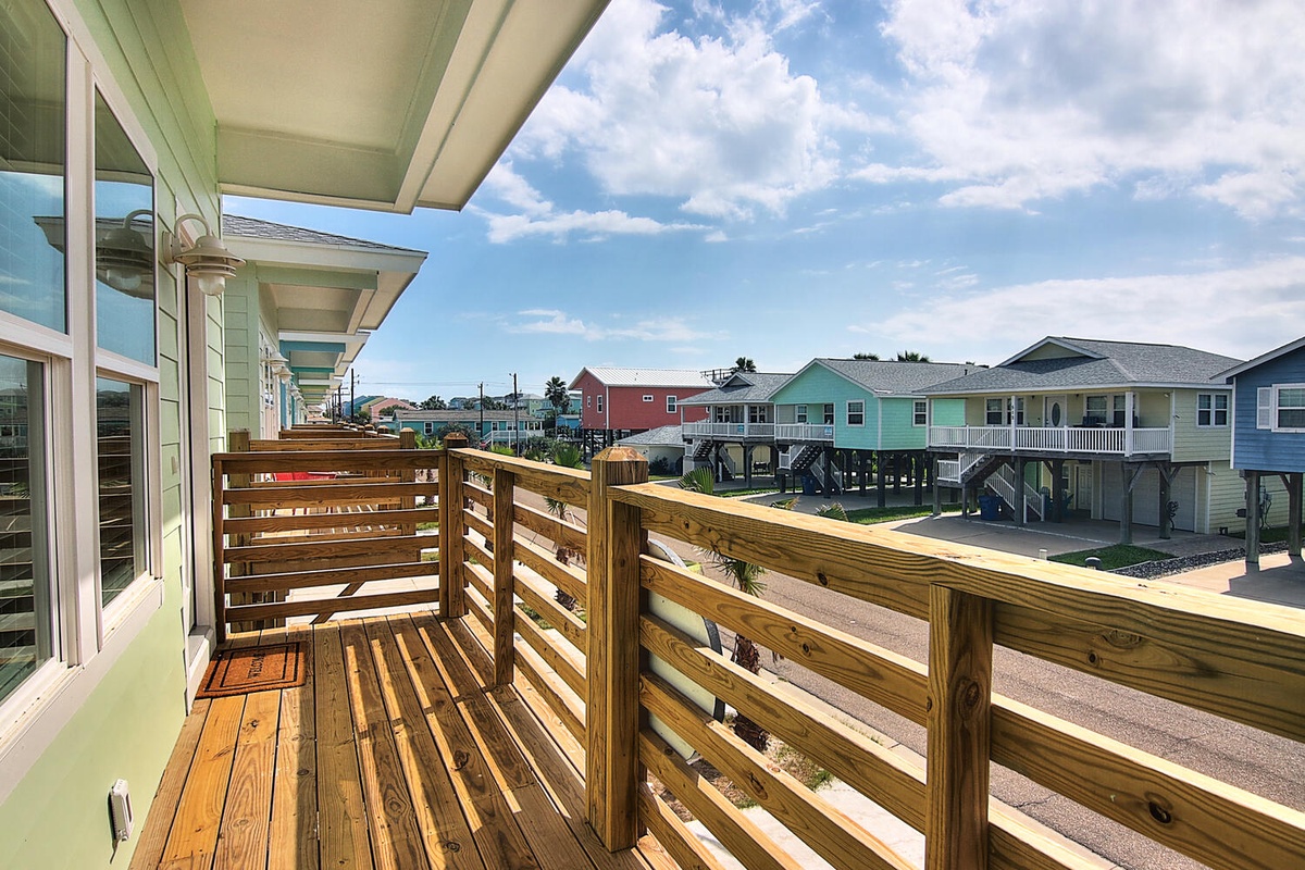 Relax on your private deck with coastal charm, where wooden railings frame colorful beach houses and blue skies create the perfect backdrop for morning coffee.