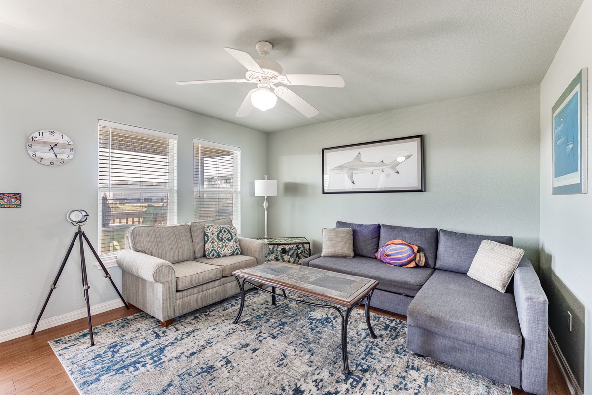 Relax in your bright living room with plush sectional seating, coastal artwork, and a ceiling fan keeping you cool.