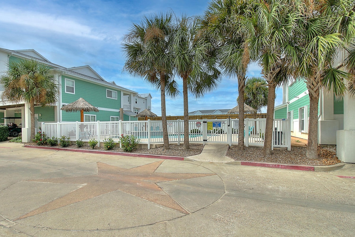 Colorful coastal property featuring bright green buildings surrounded by swaying palm trees and tropical landscaping in a sunny beachside setting.