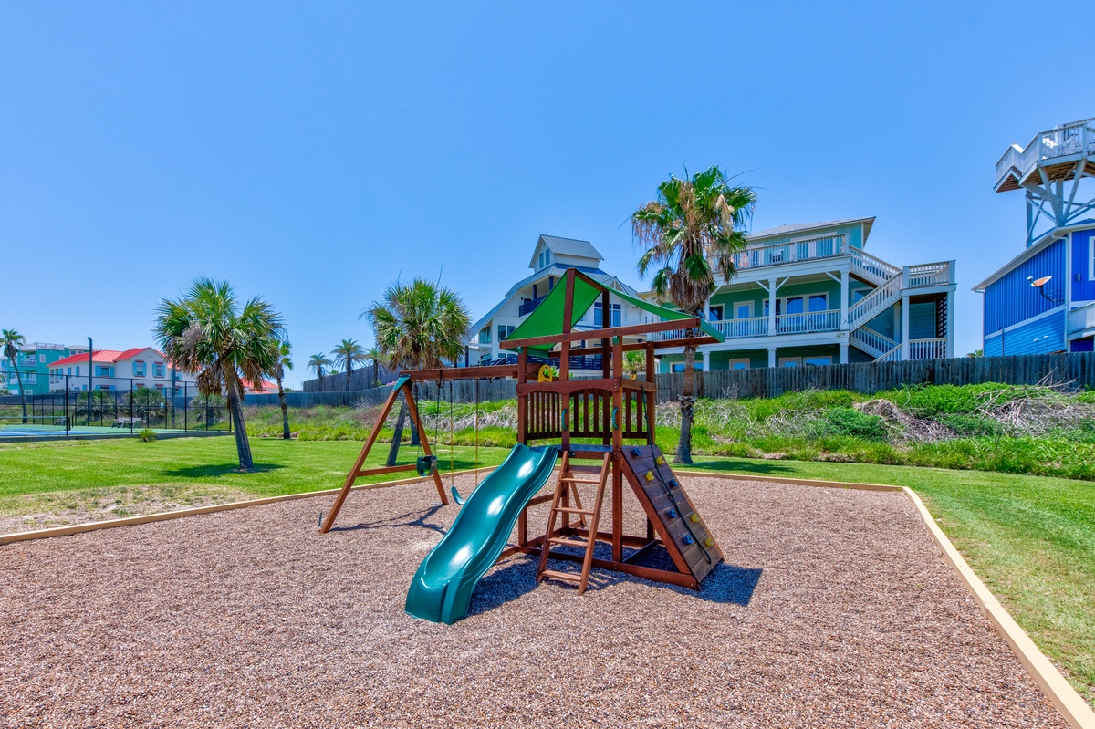Colorful beachfront playground with slides and swings surrounded by coastal vacation homes and palm trees.