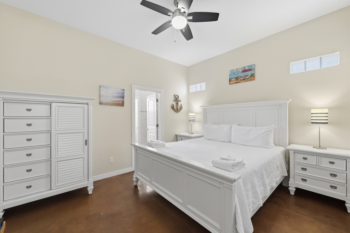 Your bright, coastal-inspired bedroom offers a plush bed dressed in soft linens, ample storage in white furniture, and a peaceful ambiance under the gentle glow of a ceiling fan—ready for restful nights after beach adventures.
