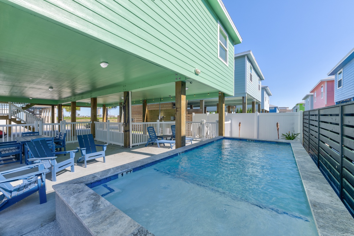 Your private oasis awaits with a sparkling pool surrounded by comfortable blue chairs, perfect for lounging under the shaded patio.