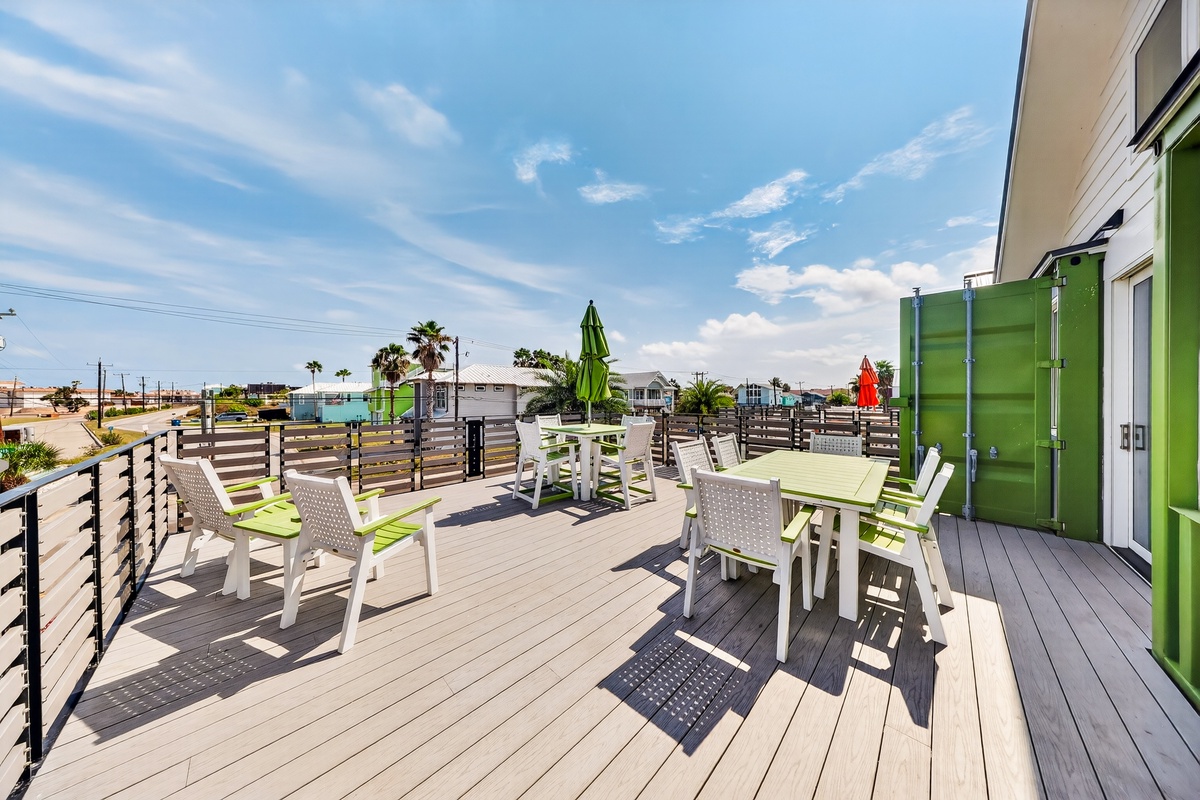The deck overlooks a quiet coastal neighborhood with palm-lined streets and calm blue skies, welcoming guests to a breezy seaside community during their arrival.