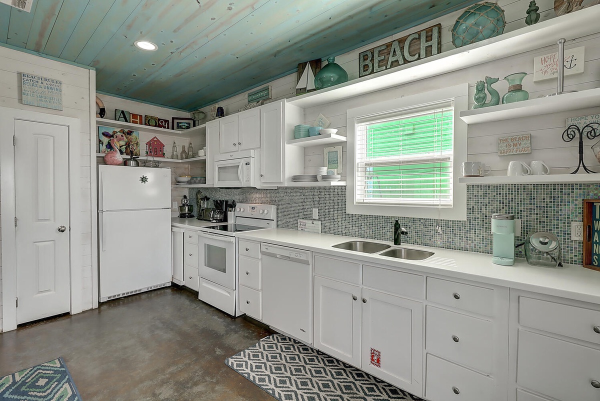 Your charming beach-themed kitchen features white cabinets, mosaic tile backsplash, and coastal decor creating a relaxing cooking space.
