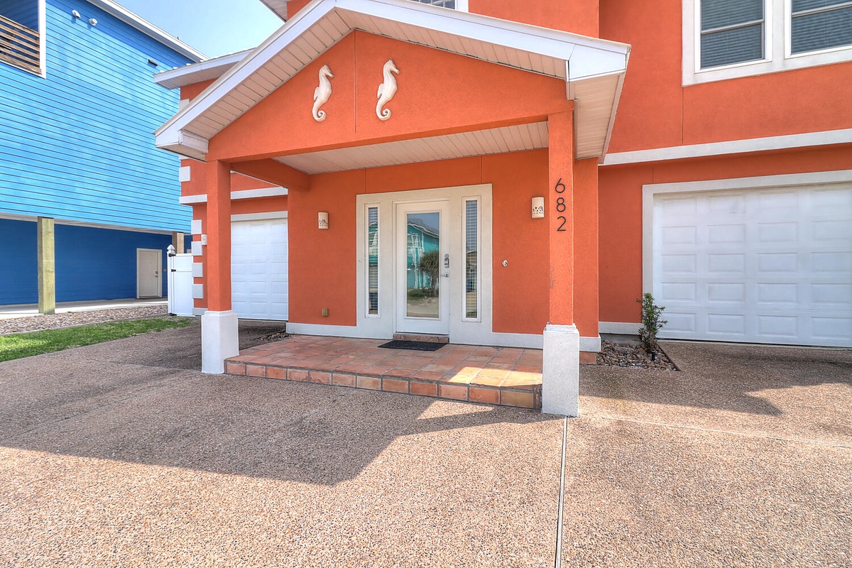 Bright coral exterior with seahorse details marks this coastal retreat. A welcoming covered entrance leads to spacious accommodations with convenient garage parking.