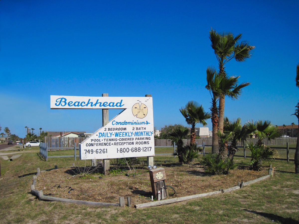 Beachhead Condominiums entrance sign featuring property amenities and contact information amid tropical palm landscaping.