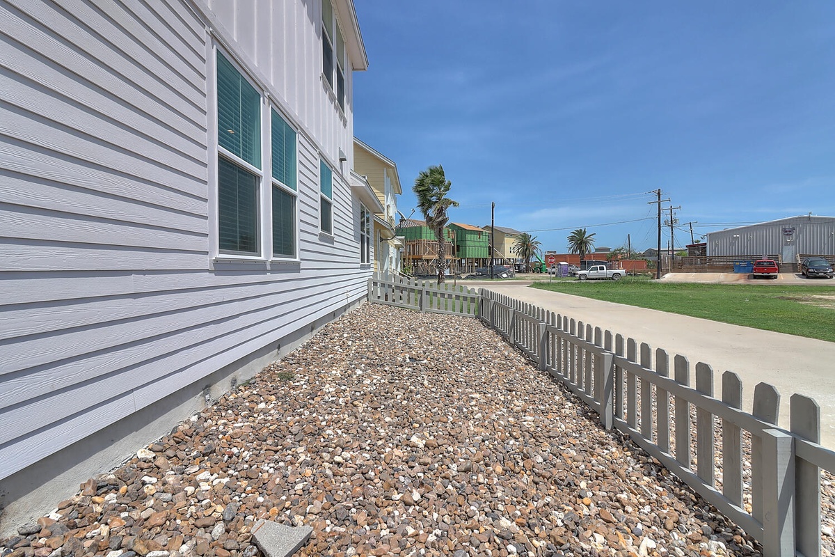 Coastal property exterior featuring white siding and charming shutters, situated in a peaceful beachside neighborhood with palm trees.