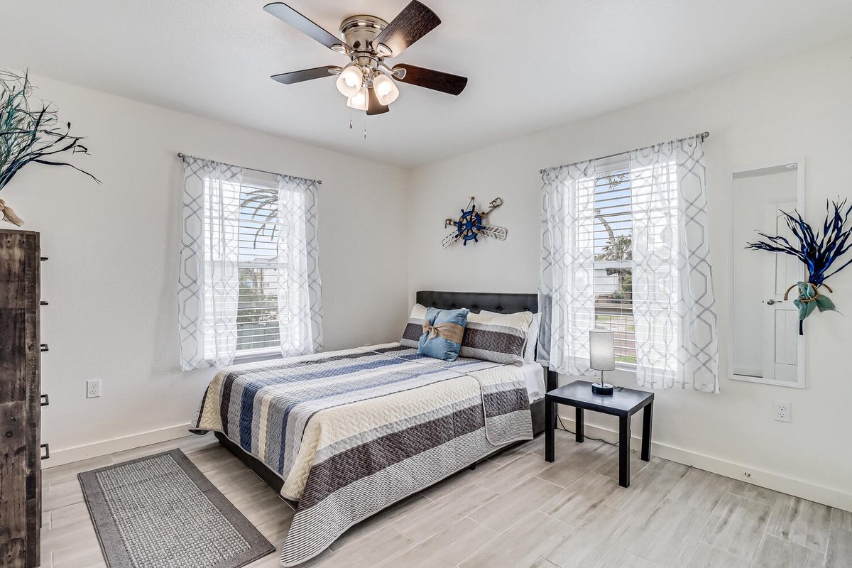Relax in your bright bedroom with coastal charm, featuring a comfy bed and ceiling fan for perfect rest.