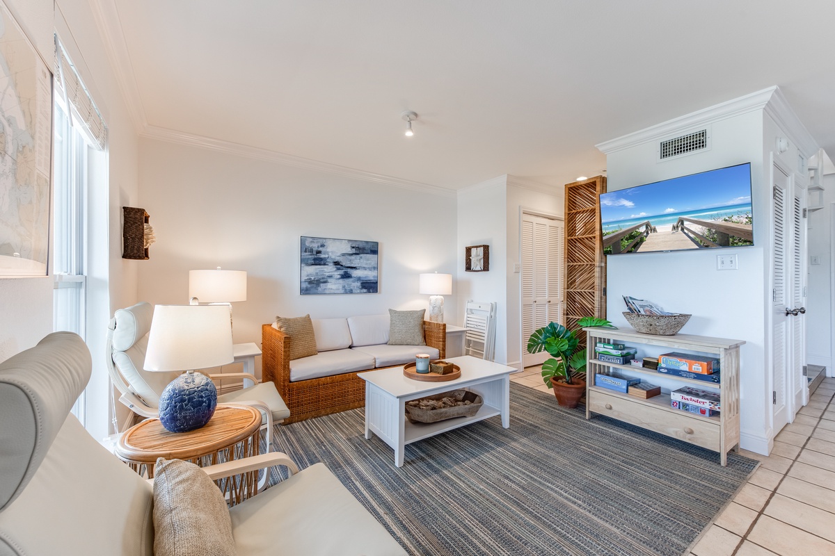 Relax in your bright coastal living room featuring comfortable seating, beach artwork, and a TV entertainment center perfect for unwinding after ocean adventures.