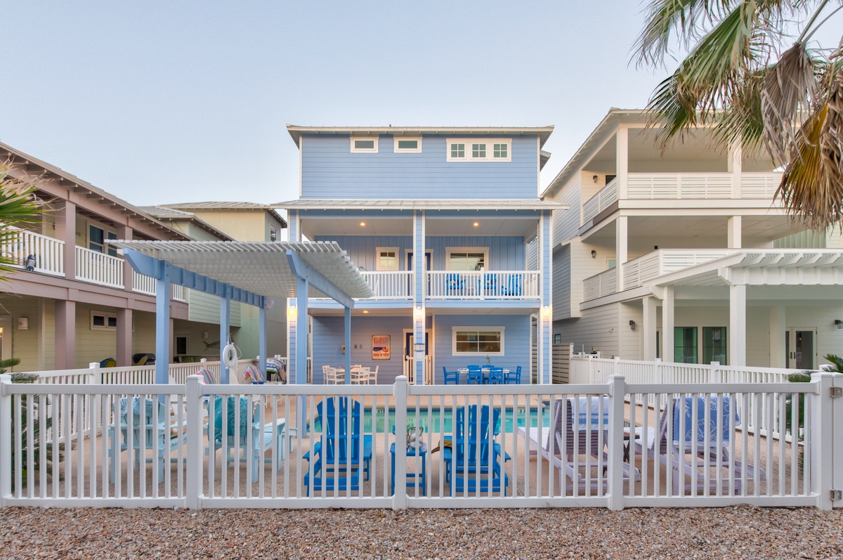 Charming blue beach house with private pool, surrounded by tropical palms and neighboring coastal properties in a peaceful vacation community.