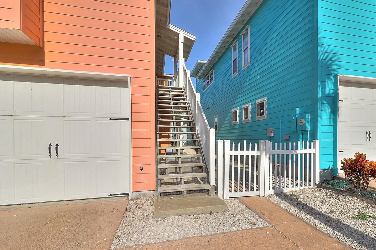 Vibrant coastal property features distinctive coral and turquoise siding with private garage access and charming architectural details.