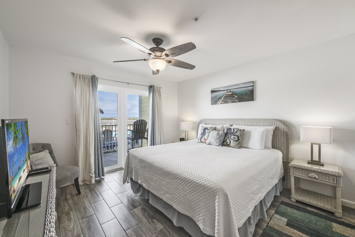 Rest easy in your bright, airy bedroom with a plush king bed, ceiling fan, flat-screen TV, and private balcony doors opening to coastal breezes.