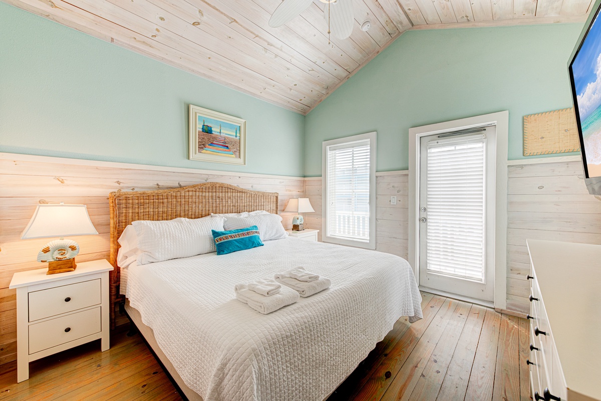 Drift off in your coastal bedroom with warm wood details, soft seafoam walls, and natural light streaming through French doors.