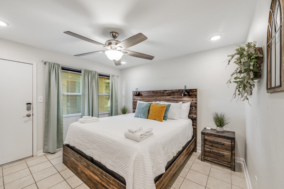Sink into your comfortable bed in this bright, airy bedroom with rustic wood touches, soft linens, and a gentle ceiling fan for perfect comfort.