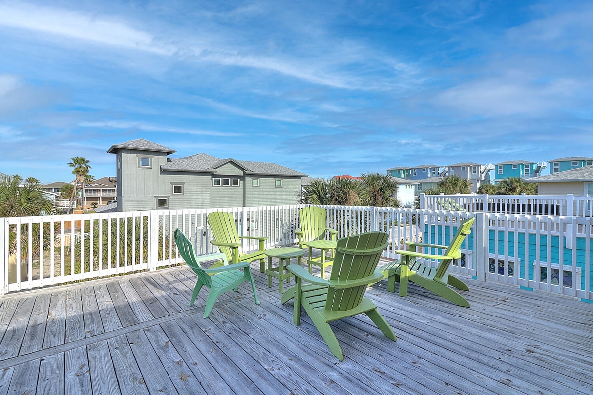 Relax in vibrant green Adirondack chairs on your private deck, surrounded by coastal charm and colorful beach houses stretching toward the horizon.