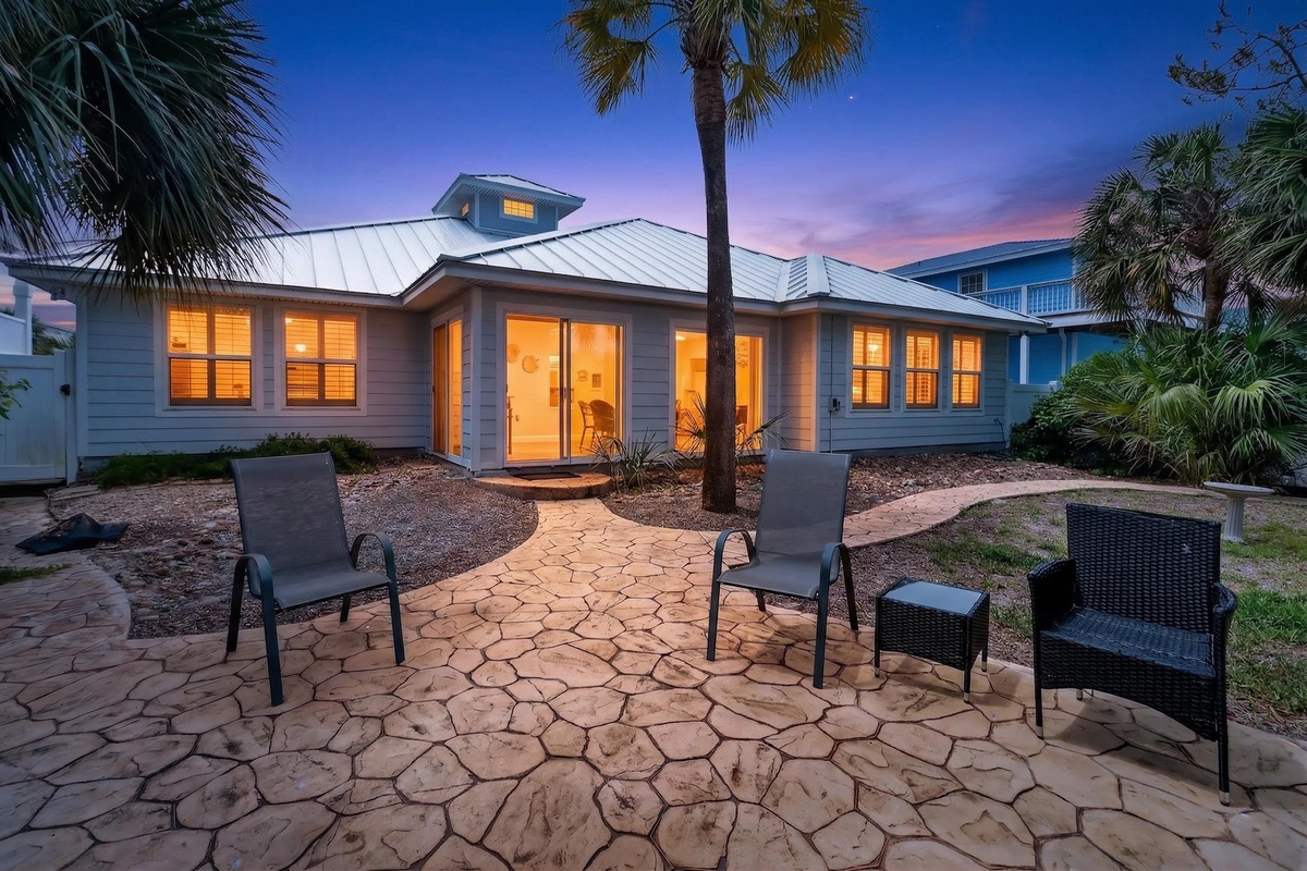Tropical paradise awaits as warm light glows from this coastal retreat surrounded by swaying palms and a stunning sunset sky.