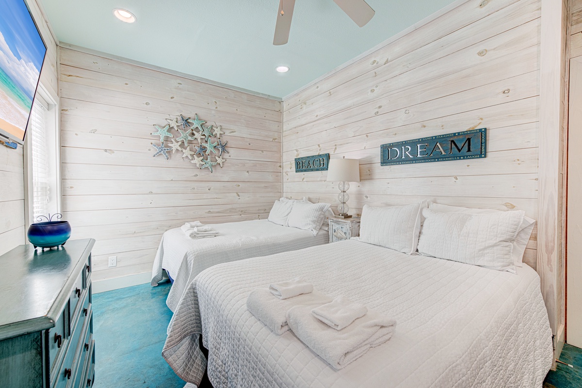 Your coastal haven awaits with two plush beds draped in crisp linens, where beach-inspired decor and soothing turquoise floors create the perfect seaside escape.