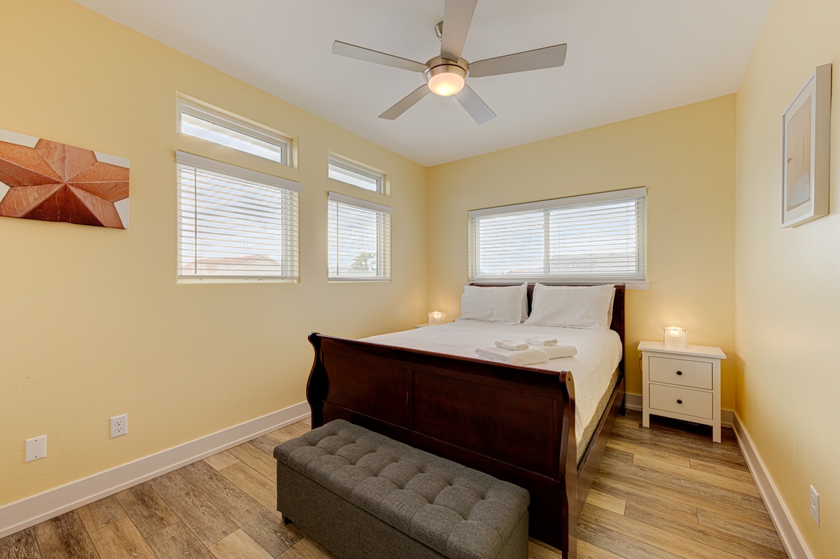 Relax in your sunny bedroom featuring a comfortable queen bed, ceiling fan, and peaceful views through multiple windows.