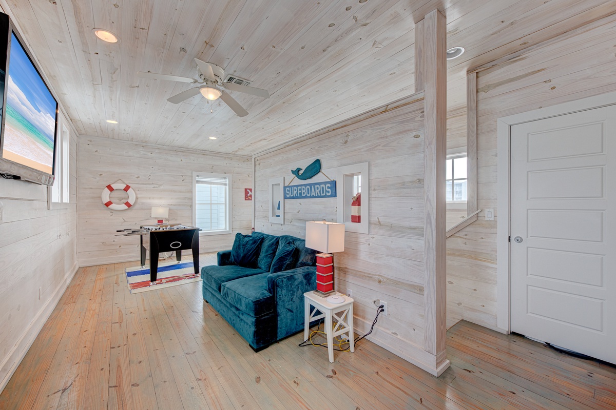 Your coastal retreat features rustic wood walls, a cozy teal sofa, and beach-themed decor that makes you feel like home by the sea.