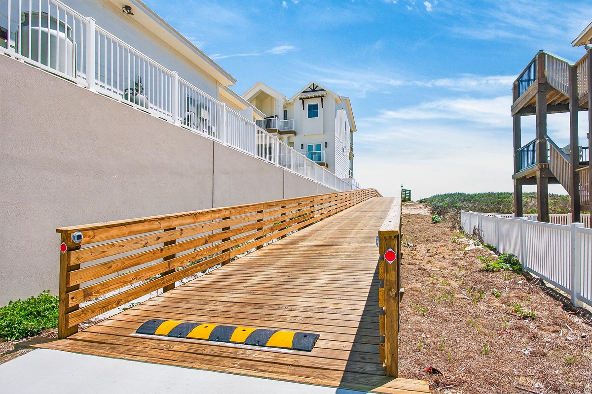Wooden boardwalk leads to beachfront vacation homes with ocean access and coastal views.