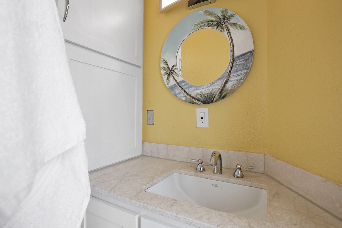 Soak away your worries in this cheerful bathroom featuring warm yellow walls and tropical palm tree mirror art that transports you to paradise.