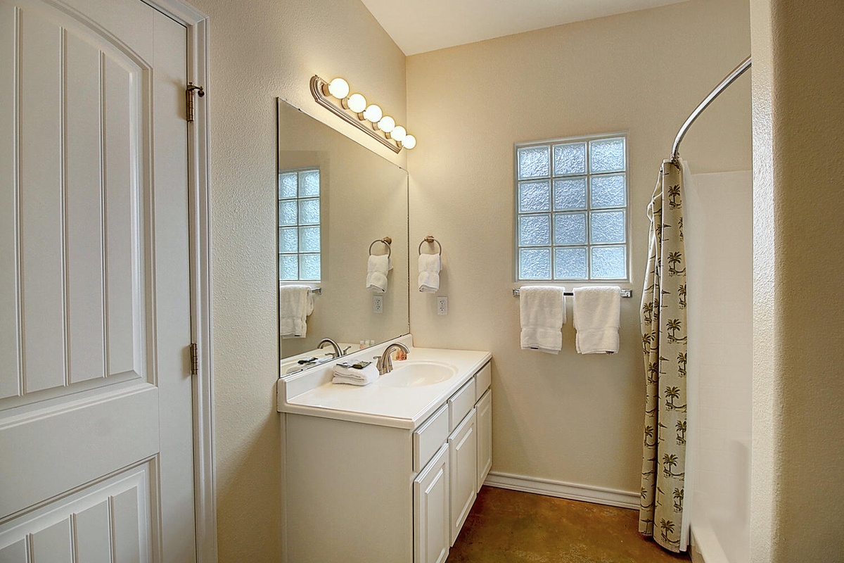 Refresh in your private bathroom with bright vanity lighting, spacious countertop, and convenient shower with tropical-themed curtain.