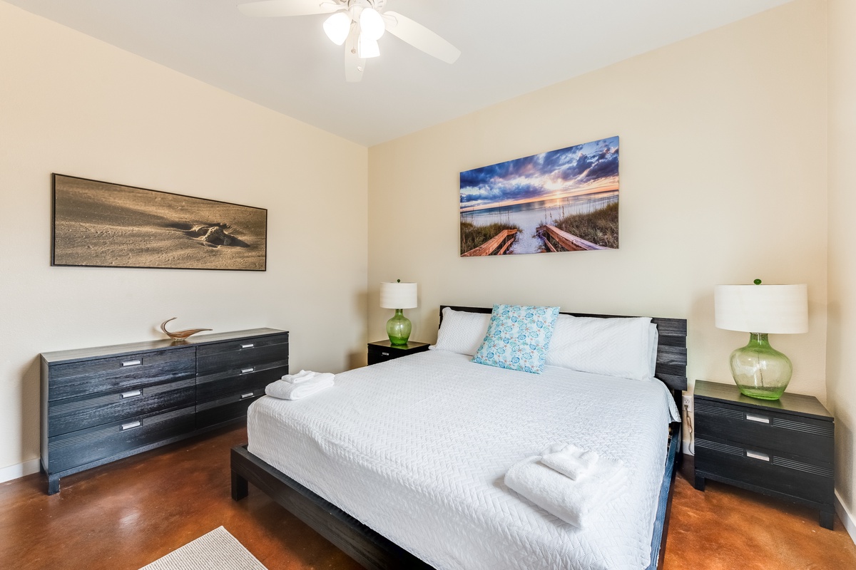 Sink into crisp white linens in your peaceful bedroom, where coastal artwork and warm lighting create the perfect retreat.