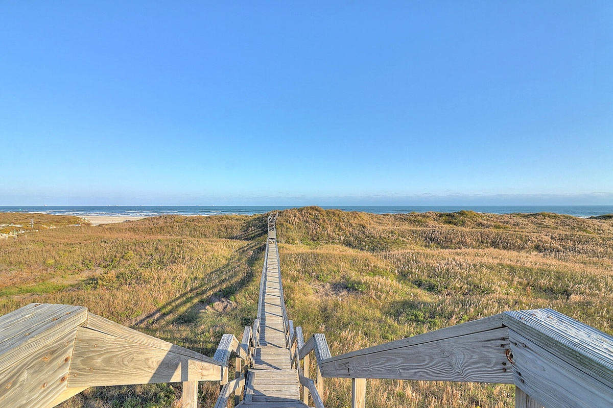 Wooden boardwalk leads through coastal dunes to the pristine beach beyond, offering stunning ocean access.
