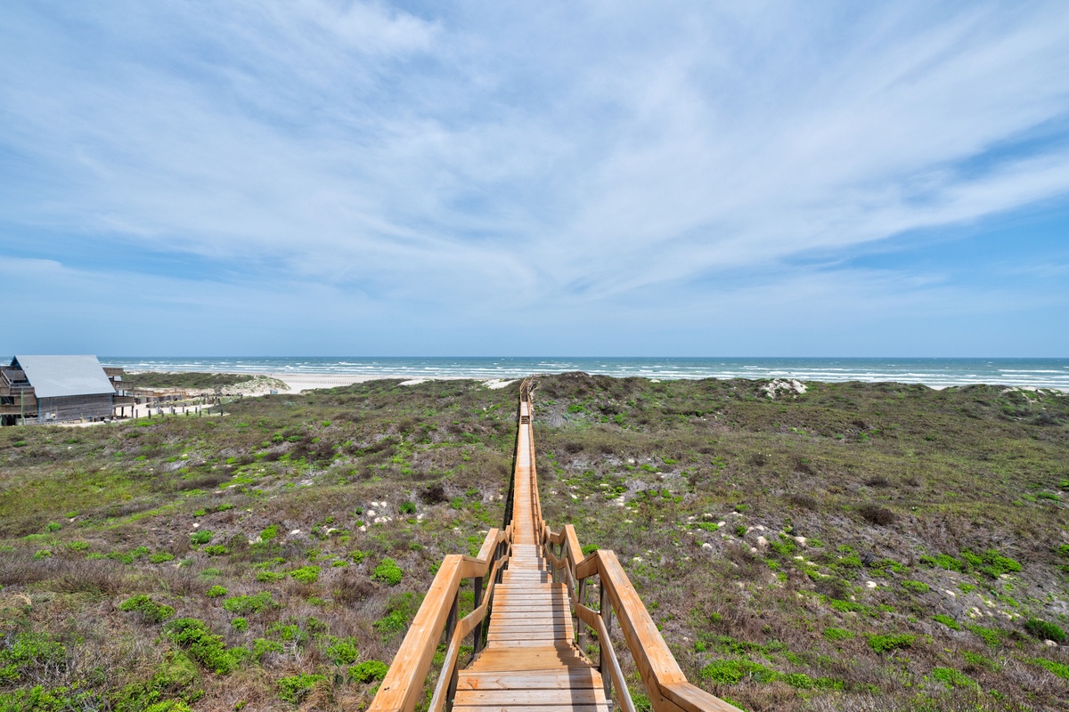 Wooden boardwalk leads through coastal dunes to pristine beach, offering direct ocean access from the property area.